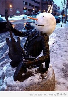 a snowman sitting on top of a rock next to a guitar