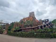 an amusement park with a roller coaster in the foreground and trees on the other side