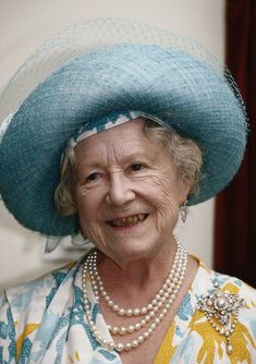 an older woman wearing a blue hat and pearls on her head, smiling at the camera