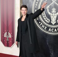 a man in a suit waves to the crowd on the red carpet at an event