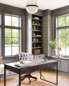 a room with two windows and a desk in the middle, surrounded by bookshelves