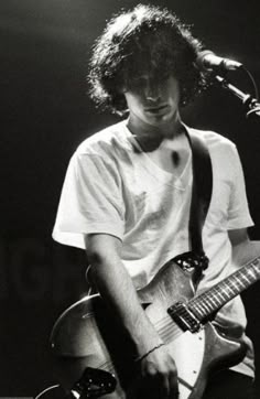 a young man with curly hair playing an electric guitar in front of a microphone on stage