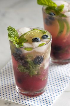 two glasses filled with blueberries and limeade on top of a white tile counter