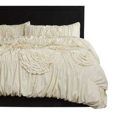 a white bed with ruffled sheets and pillows on it's headboard, in front of a white background