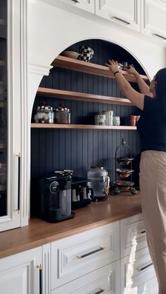 a woman standing on top of a kitchen counter next to a shelf filled with pots and pans