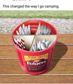 a red bucket filled with silverware on top of a wooden table next to grass