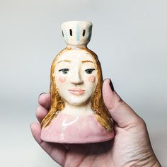 a hand holding a ceramic figurine with a hat on it's head