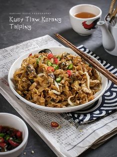 a white bowl filled with food next to chopsticks and a cup of tea