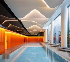 an indoor swimming pool surrounded by tall windows and orange panels on the ceiling above it