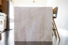 a white marble counter top sitting in a kitchen next to a stove and chairs on the floor