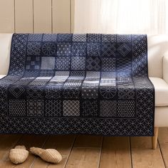 a couch covered in a blue and white quilt next to two slippers on the floor