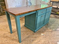 a blue kitchen island with wooden top in an unfinished room