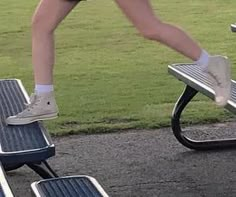 a person in tennis shoes stepping on a park bench with their feet up and running