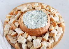 a bowl of dip surrounded by bread on a wooden platter with white napkins