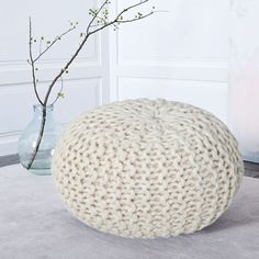 a white knitted poufce sitting on top of a rug next to a vase