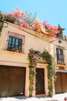 an old building with flowers growing on the roof and windows over the garage doors in front of it