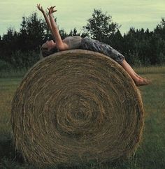 a boy laying on top of a hay bale in the middle of a field