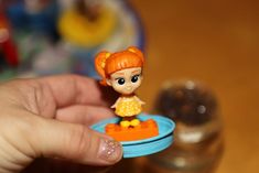 a person holding a tiny doll on top of a blue plate with an orange dress