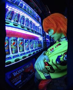 a man with red hair and green shirt next to slot machines in a dark room