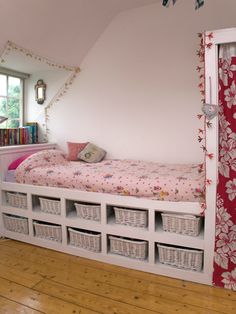 there is a bed with baskets under it in the room that has pink walls and wooden flooring