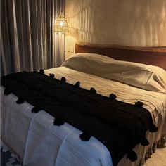 a bed with white sheets and black pom poms on the headboard is lit by a lamp