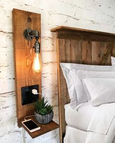 a bed with white sheets and pillows next to a wooden headboard, light fixture and phone