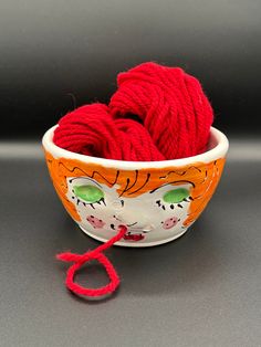 a bowl with yarn in it and a pair of red scissors on the table next to it