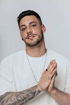 a man with tattoos on his arm and hands folded in front of him, looking at the camera