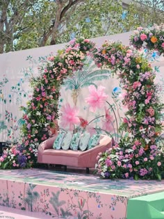 a pink couch sitting on top of a stage covered in lots of flowers and greenery