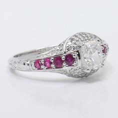 an oval cut diamond ring with pink and white stones on the band, set in 18k white gold