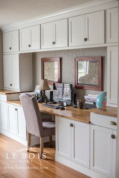 a home office with white cabinets and wood flooring is pictured in this image, there are two framed pictures on the wall above the desk