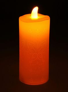 an orange lit candle with a butterfly design on the front and side, in dark background