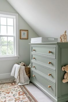 a baby's room with a green dresser and teddy bear on the top shelf