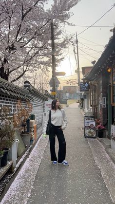 a woman standing on the sidewalk in front of a building with cherry blossom trees around her