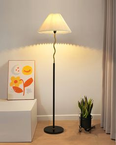 a floor lamp next to a potted plant in a room with a white wall