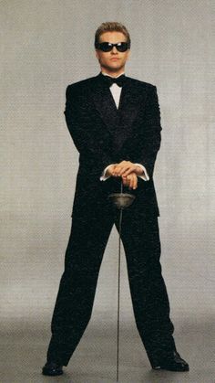 a man in a tuxedo and sunglasses is holding a cane with both hands