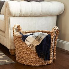 a basket sitting on top of a wooden floor next to a white couch with pillows