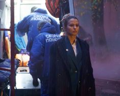 a woman is walking down the street in front of some people wearing blue jackets and holding an umbrella