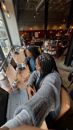 two women sitting at a table with laptops in front of them, looking out the window