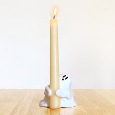 a candle with a ghost face on it sitting in front of a white wall and wooden floor