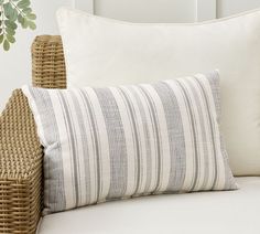 a close up of a pillow on a bed with wicker furniture and plants in the background