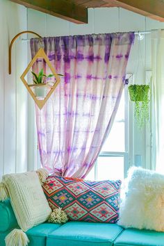 a living room filled with lots of furniture next to a window covered in purple and white curtains