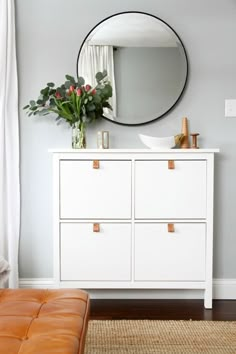 a white dresser and mirror in a room with a brown leather bench next to it