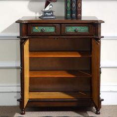 a wooden cabinet with two drawers and a clock on it's top, in front of a white wall