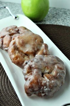 three glazed donuts on a white plate with an apple in the backround