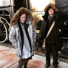 two people standing next to each other in front of a train