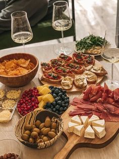 a wooden table topped with different types of food and wine glasses on top of it