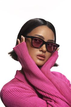 a woman in pink sweater and black sunglasses with her hand on her head, looking off to the side