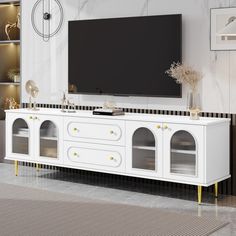 a white entertainment center with gold accents and a flat screen tv mounted on the wall