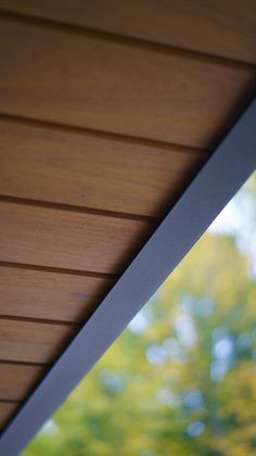 a bird is perched on the side of a wooden roof with trees in the background